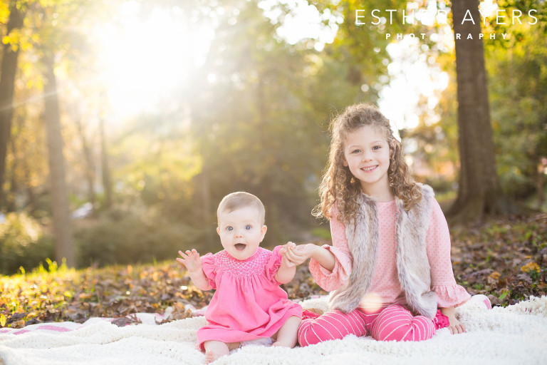 two sweet sisters holding hands on a blanket in a park at sunset