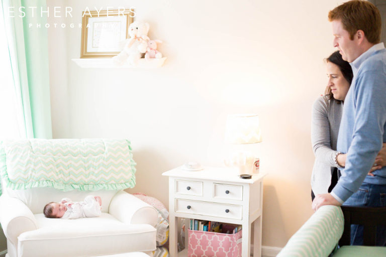 Newborn Baby Girl on chair in nursery with parents looking on