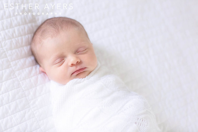 Newborn Baby Girl smiling wrapped in blanket on Bed