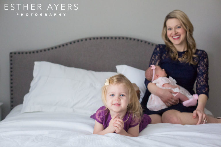 big sister on bed with mom and newborn baby girl