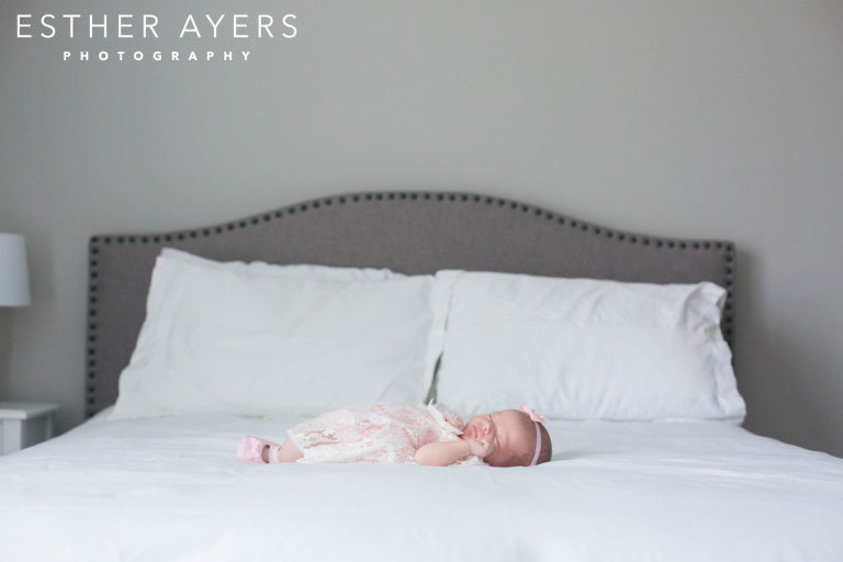 newborn baby girl in pink dress and headband on a bed