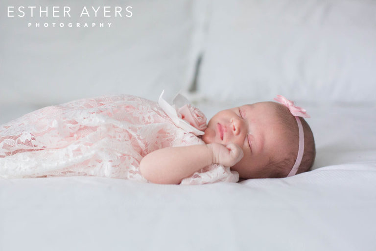 newborn baby girl in pink dress and headband on a bed