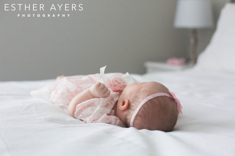 newborn baby girl in pink dress and headband on a bed
