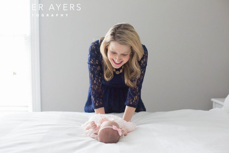 Mom with newborn baby girl wrapped in a pink swaddle on a bed