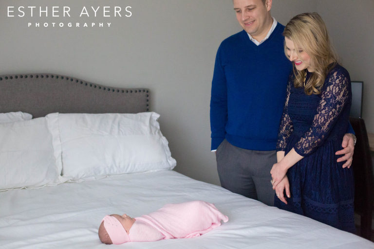 Mom and dad with newborn baby girl wrapped in a pink swaddle on a bed