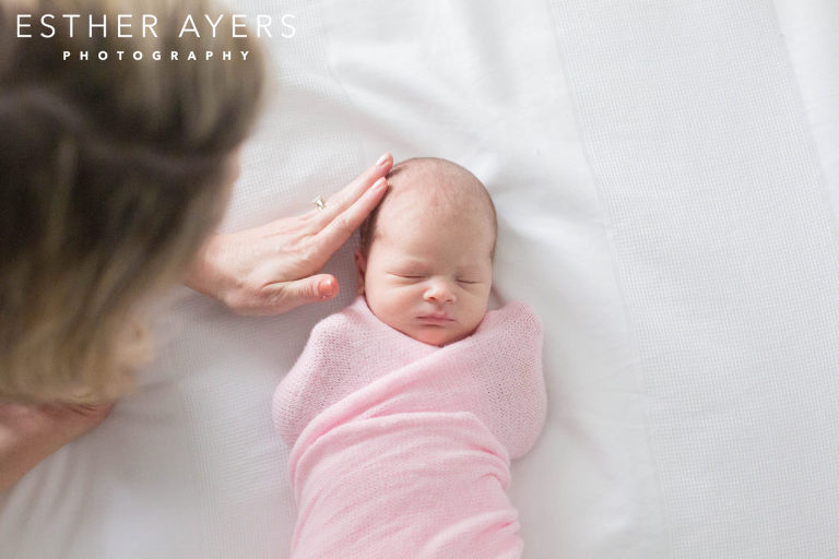 Mom with newborn baby girl wrapped in a pink swaddle on a bed