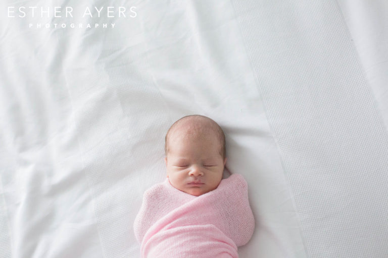 newborn baby girl wrapped in a pink swaddle on a bed