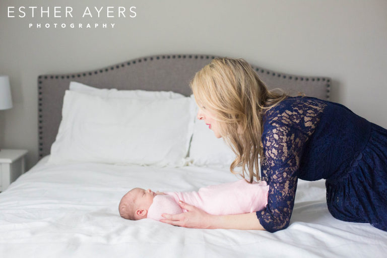 Mom with newborn baby girl wrapped in a pink swaddle on a bed