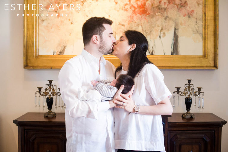 mom and dad kissing and holding newborn baby boy