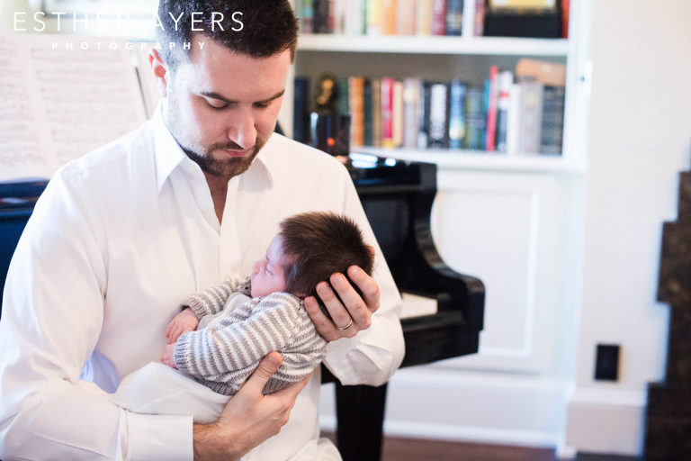 new dad looking at newborn baby boy next to piano and books