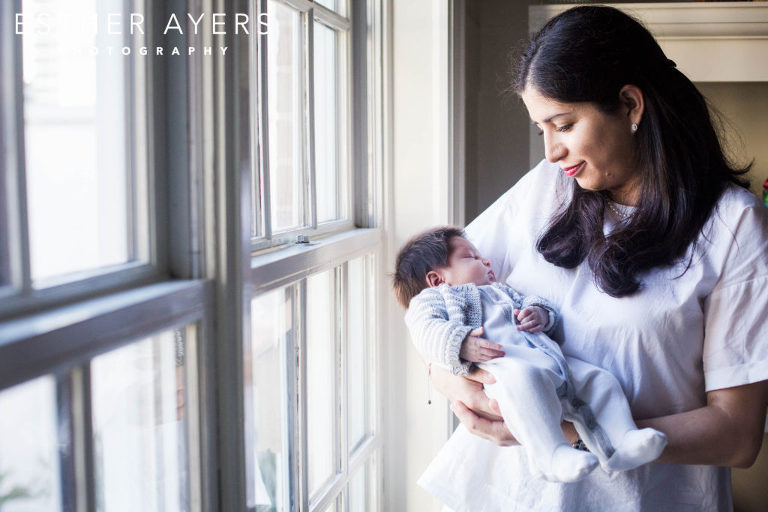 new mom looking at newborn baby boy next to window